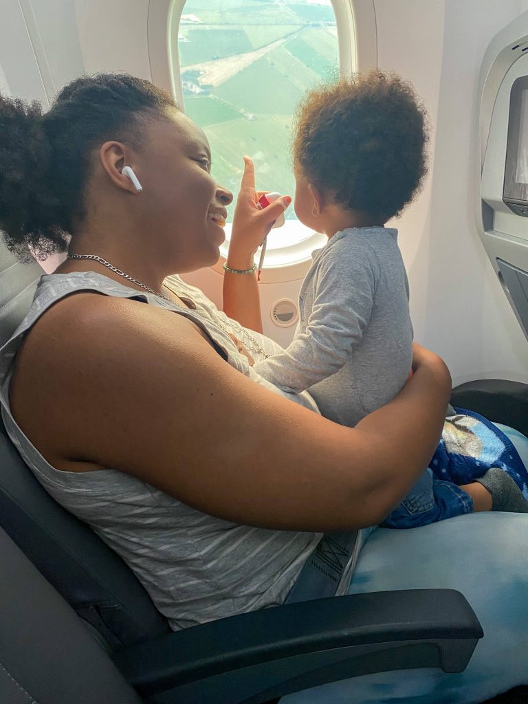 Tips for flying with a baby. A woman points out to window on an airplane as an infant child looks out the window. 